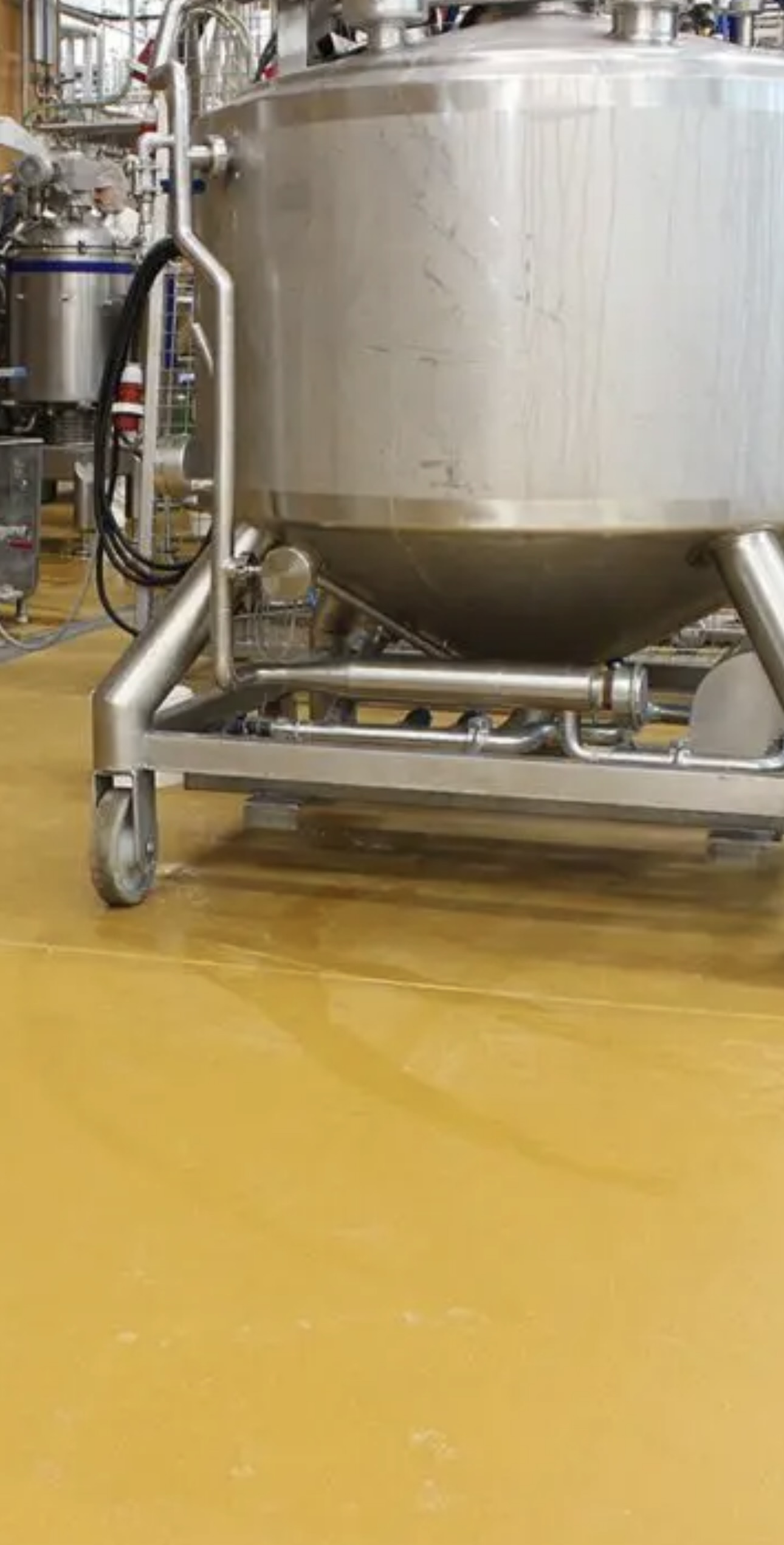 Stainless steel vat standing on a yellow epoxy-coated floor in a dairy plant